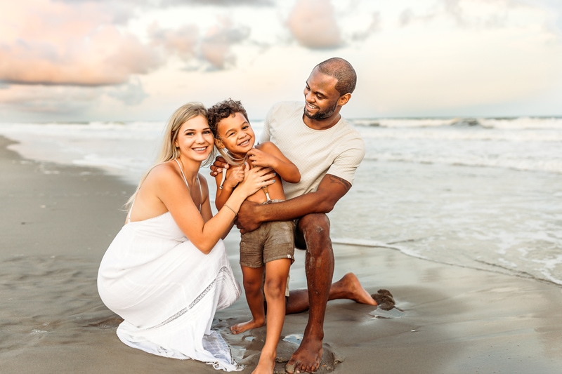 Family Photographer, a mother and father stand with their young son smiling at the beach