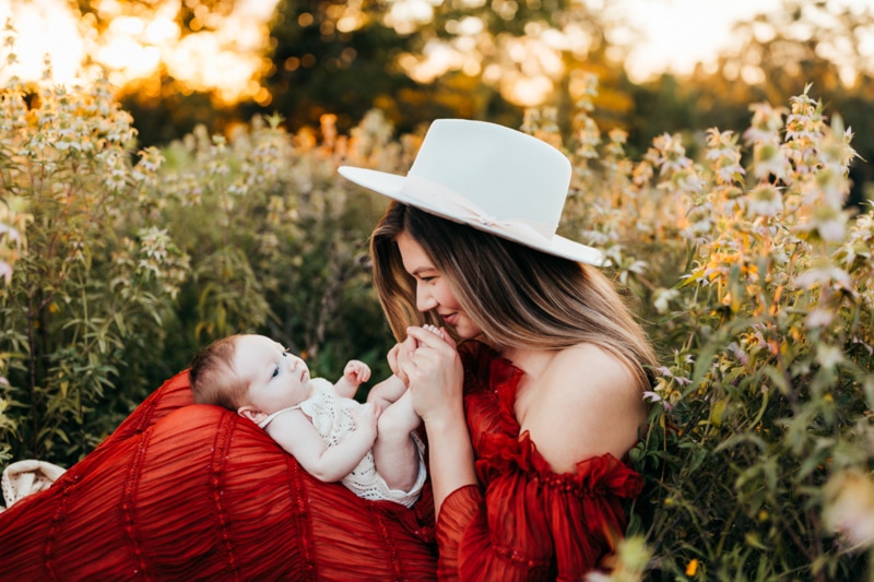 Newborn Photographer, a Mother in red dress sits in flowers with her baby