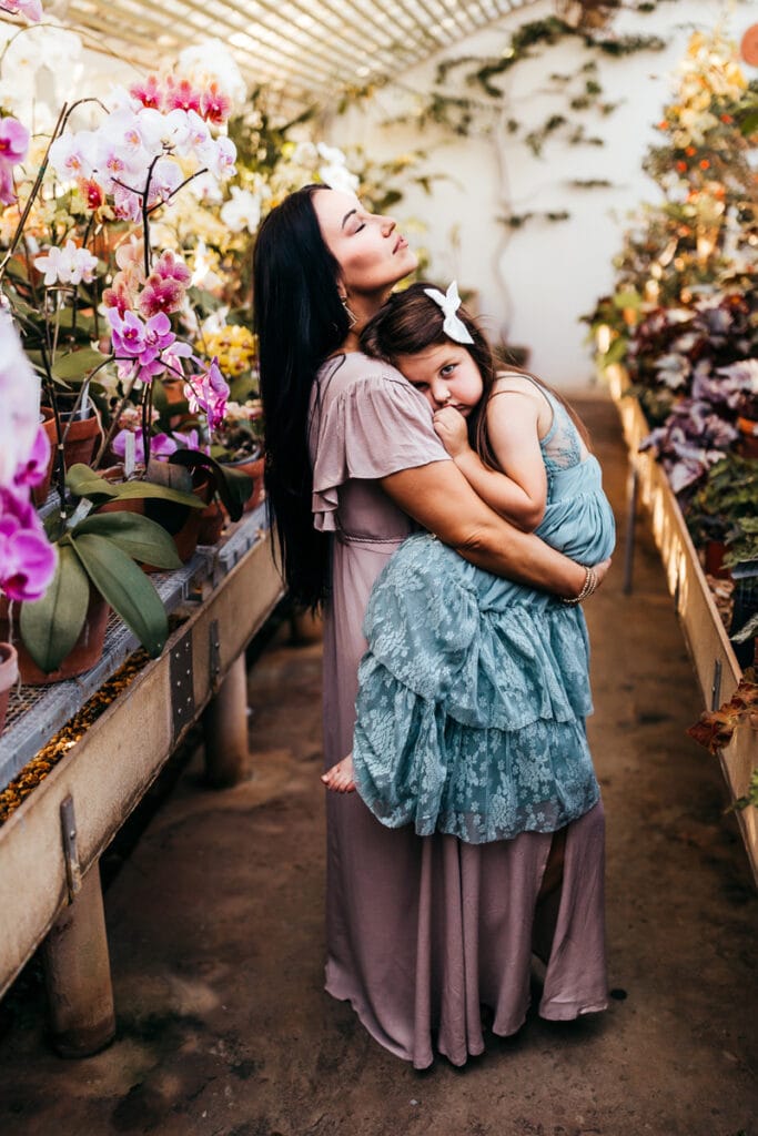 Family Photographer, a mother holds her daughter in a flower-filled green house